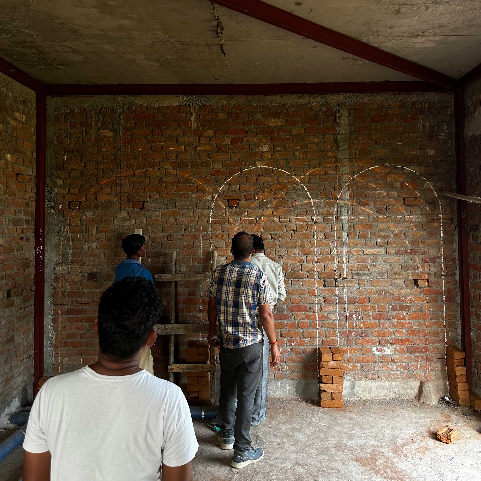 A group of workers indoors examining a brick wall marked with white chalk outlines for three arched doorways.