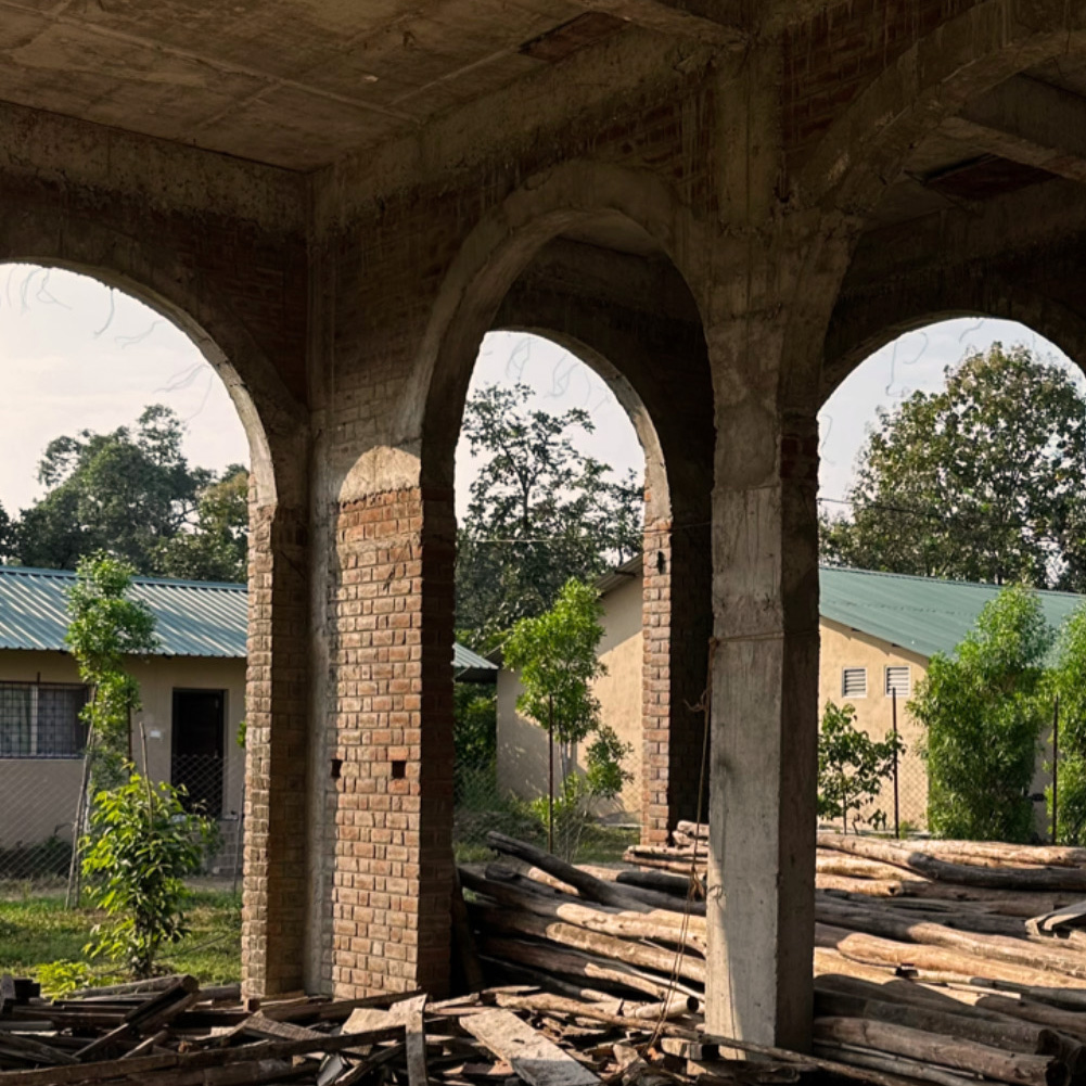 A concrete and brick building under construction with prominent arched openings overlooking a rural landscape.